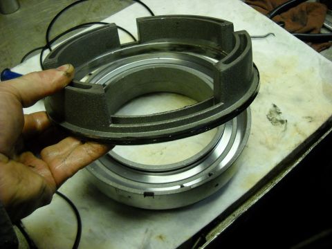 1993 Ford C-150 (Centurion Conversions) - A mechanic's hand holds a metal transmission part above a similar component on a cluttered workbench.