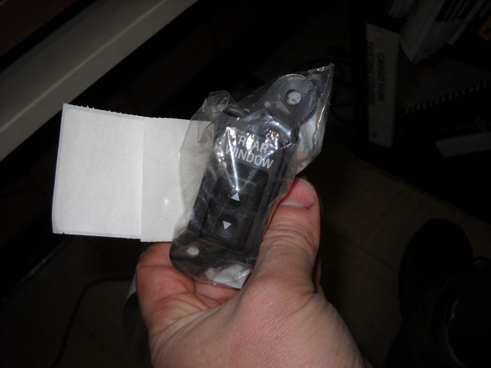 Hand holding a new rear window switch in plastic packaging. Text on the switch reads 'REAR WINDOW'