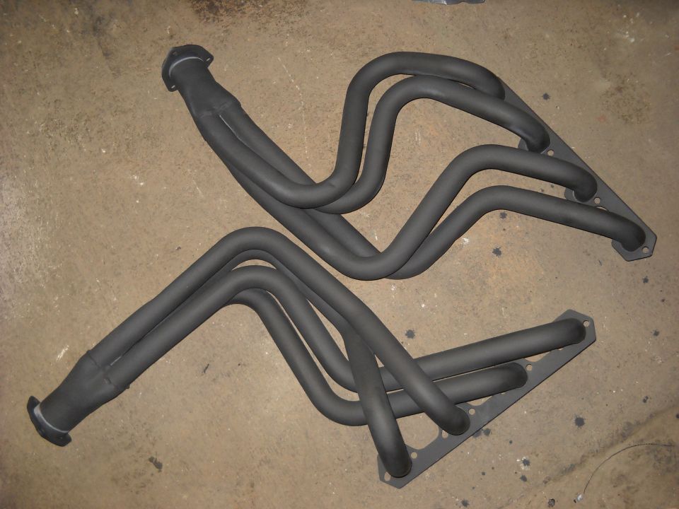 Two black exhaust manifolds with multiple pipes, lying on a concrete floor
