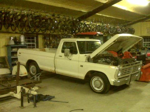 1973 Ford F-100 - White 1973 Ford F-100 pickup truck parked inside a garage with its hood open.