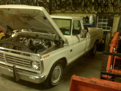 1973 Ford F-100 - A white 1973 Ford F-100 pickup truck is parked inside a garage with its hood open.