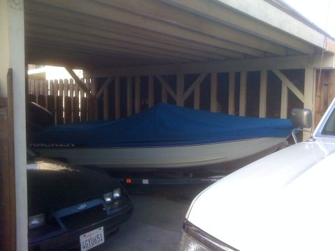 1968 Ford Mustang - A boat covered in blue is parked in a carport, partially obscured by a dark car and a white vehicle.