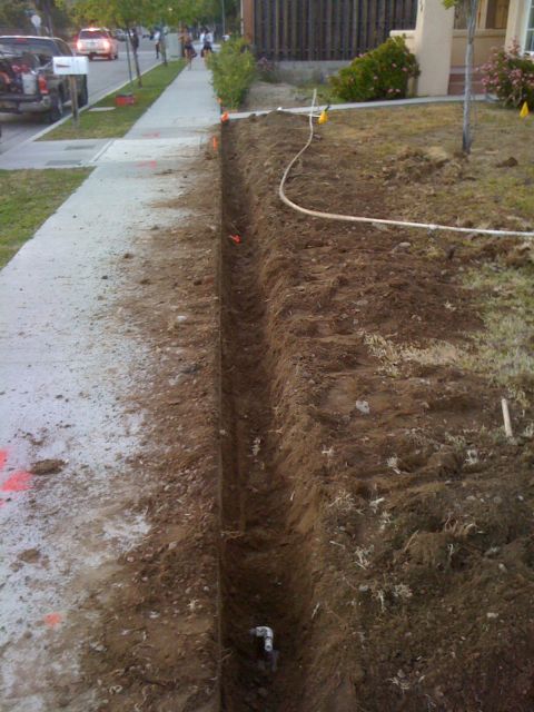 1968 Ford Mustang - A long trench has been dug next to a sidewalk, with a white pipe visible within the trench.