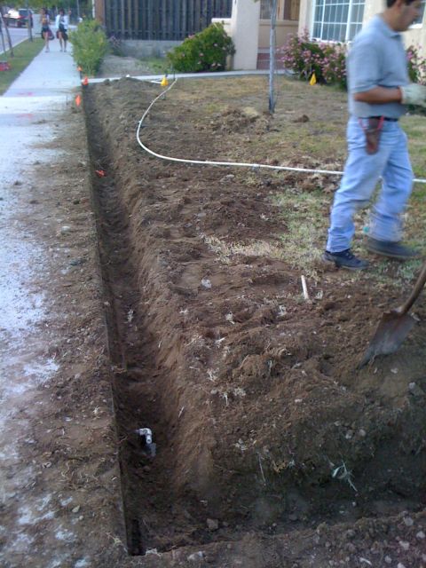 1968 Ford Mustang - A trench is being dug in a residential yard, with a person visible in the background and a pipe laid out.