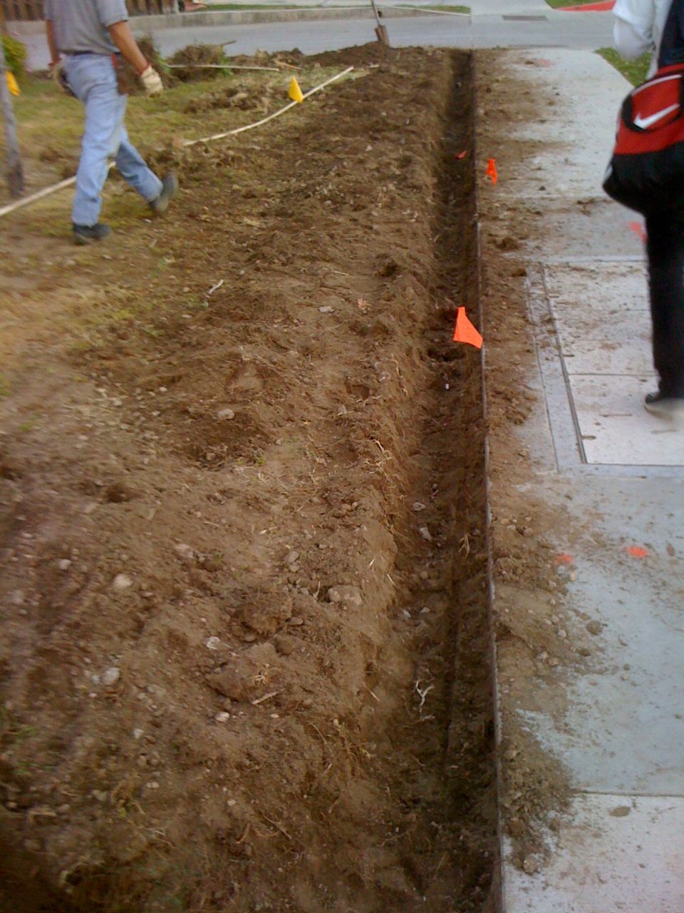 Construction trench dug next to a sidewalk with two workers visible