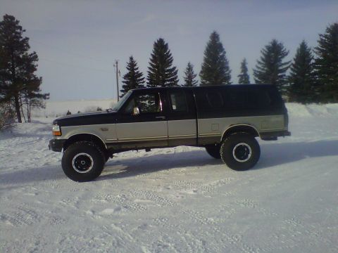 1994 Ford F-150 - A lifted Ford F-150 pickup truck with a camper shell sits in a snowy landscape under a bright sky.