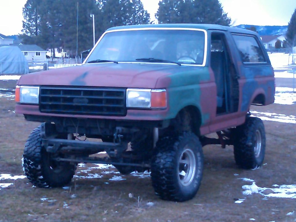 Lifted 1987 Ford Bronco with camouflage paint, missing passenger door and rear quarter panel