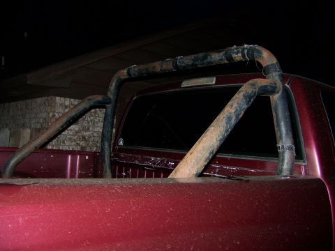 1992 Jeep YJ - The rear of a red pickup truck is shown with a rusty roll bar installed in the bed.