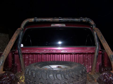 1992 Jeep YJ - The rear of a maroon truck is shown with a spare tire and a rusty roll bar.
