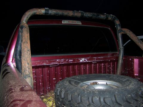 1992 Jeep YJ - Rear view of a red pickup truck bed a rusty roll bar and a spare tire mounted inside.