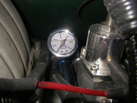 1990 Ford Bronco - Under-hood close-up of a BBK fuel pressure gauge, 0-60 psi white face in a chrome bezel, mounted on a blue-anodized fitting at the fuel rai…