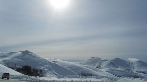 1989 Ford Bronco - A lone white SUV travels along a snow-covered road, dwarfed by vast, undulating snow-covered hills under a bright sky.