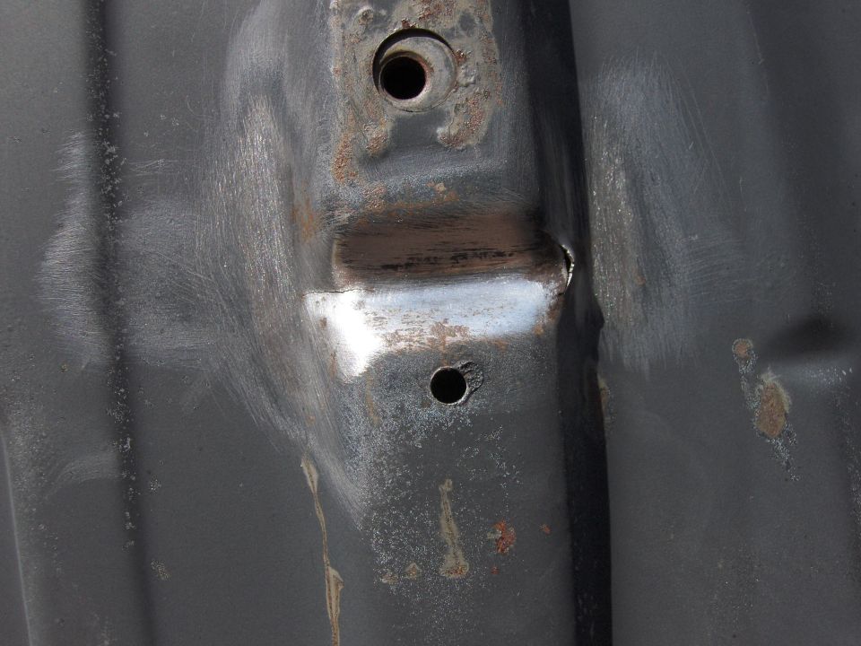 rusted metal bracket with two bolt holes and evidence of grinding