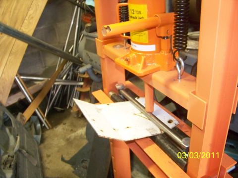 1989 Ford Bronco - An orange hydraulic press is shown in a cluttered workshop environment with various metal parts and tools.