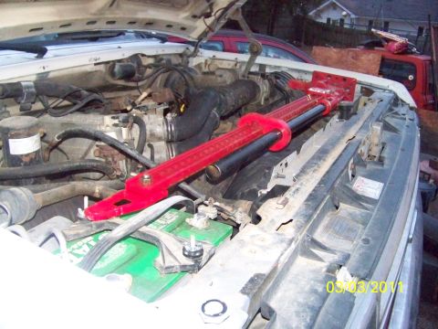 1989 Ford Bronco - A red hi-lift jack is positioned over the battery in the engine bay of a vehicle.
