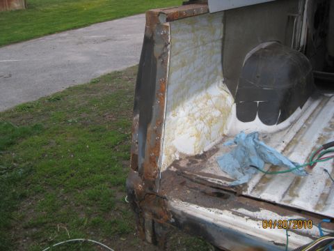1983 Ford Bronco - The rear corner of a white vehicle displays significant rust and damage, with wiring exposed.