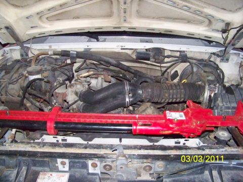1989 Ford Bronco - Open engine bay of a truck with the radiator and grille support removed, showing the flexible intake ducting, valve cover, hoses and wiring…
