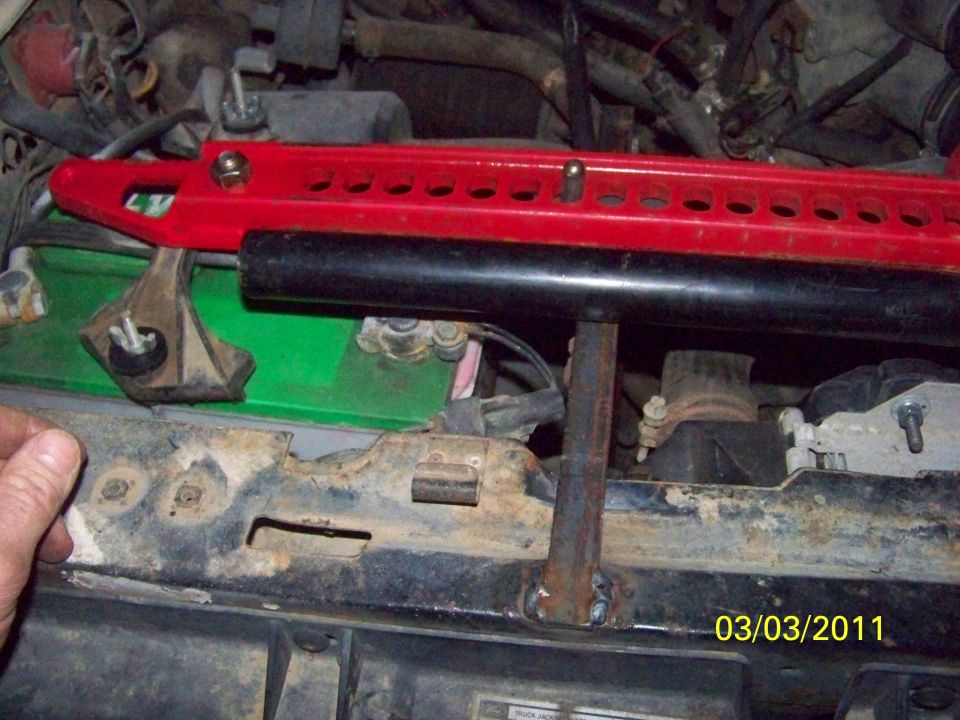 Red high-lift jack bar across a truck core support next to a green battery
