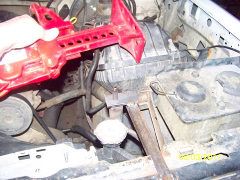 1989 Ford Bronco - A hand holds a red high-lift jack up over a truck's engine bay to check clearance against a welded steel mounting tab on the radiator suppo…