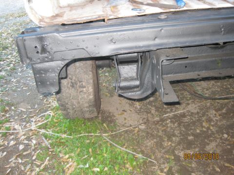 1983 Ford Bronco - Low-angle shot of the rear quarter and inner fender area of a stripped SUV body, with the sheetmetal and frame rail freshly coated in thick…