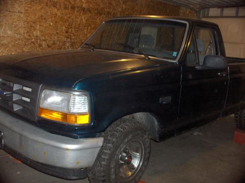 1994 Ford F-150 - This dark green Ford F-150 pickup truck is viewed from the front passenger side, parked inside a garage.