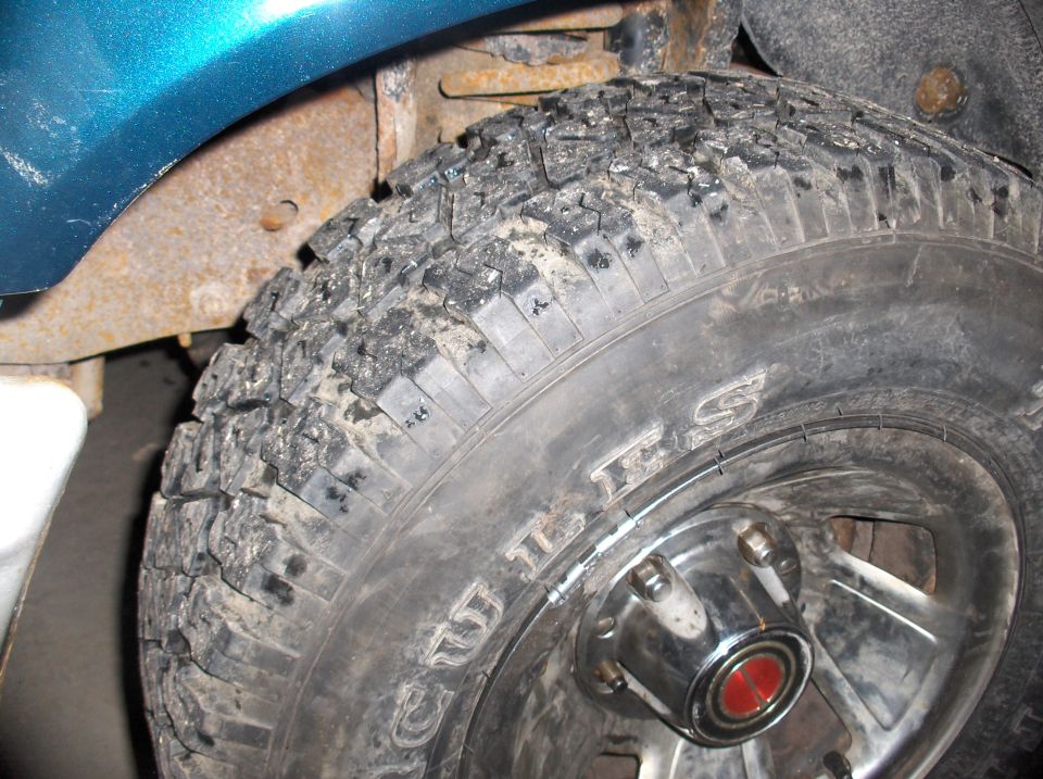 Close-up of a dirty tire with visible text and a rusty wheel well