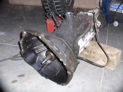 1994 Ford F-150 - Transmission assembly resting on wooden blocks, with a tire visible in the background.