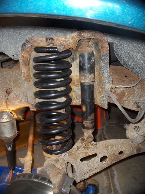 1994 Ford F-150 - Close-up view of the front suspension system, showing a coil spring and shock absorber with significant rust.