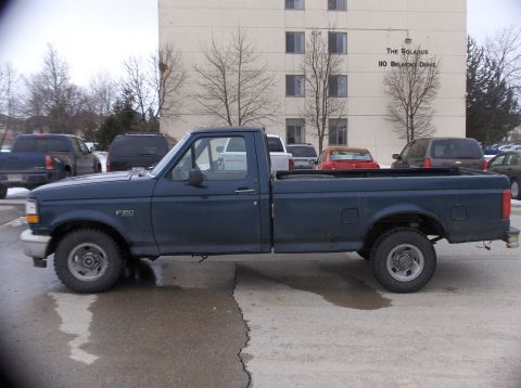 1994 Ford F-150 - A dark blue 1994 Ford F-150 pickup truck is seen from the side. The F-150 badge is visible on the fender.