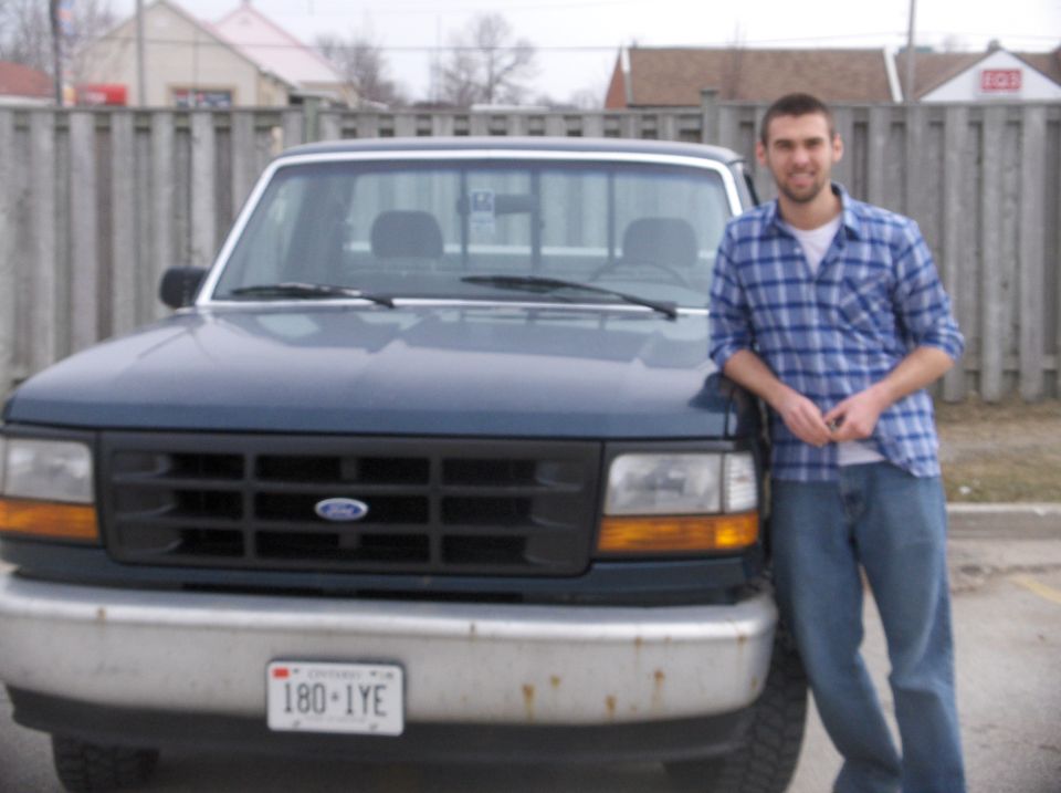 Man leaning on a 1994 Ford F-150 truck, front view. License plate reads 180-IYE