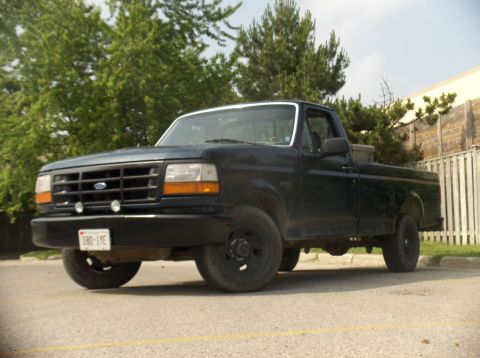 1994 Ford F-150 - This black Ford F-150 pickup truck is parked outdoors with trees and a wooden fence visible.