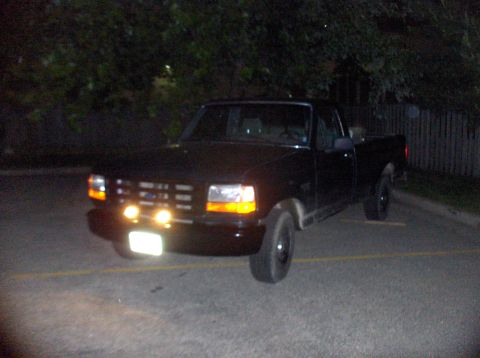 1994 Ford F-150 - A black 1994 Ford F-150 pickup truck is parked at night, viewed from the front three-quarter angle.