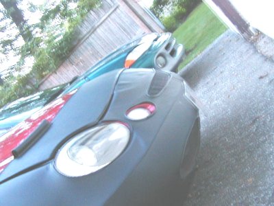 1997 Ford Taurus - A 1997 Ford Taurus with a dark gray cover over its front end is parked next to a teal car.