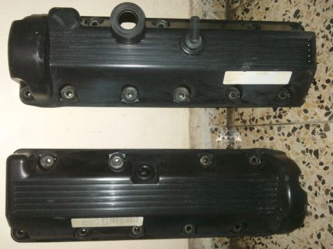 1998 Ford Crown Victoria - Two black valve covers are shown, one with a rubber hose fitting, against a tiled background.