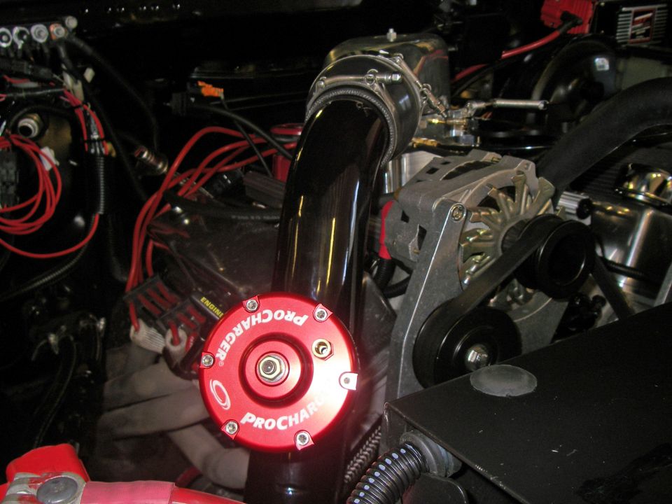 Red ProCharger cap with visible text, connected to black intake piping and engine components