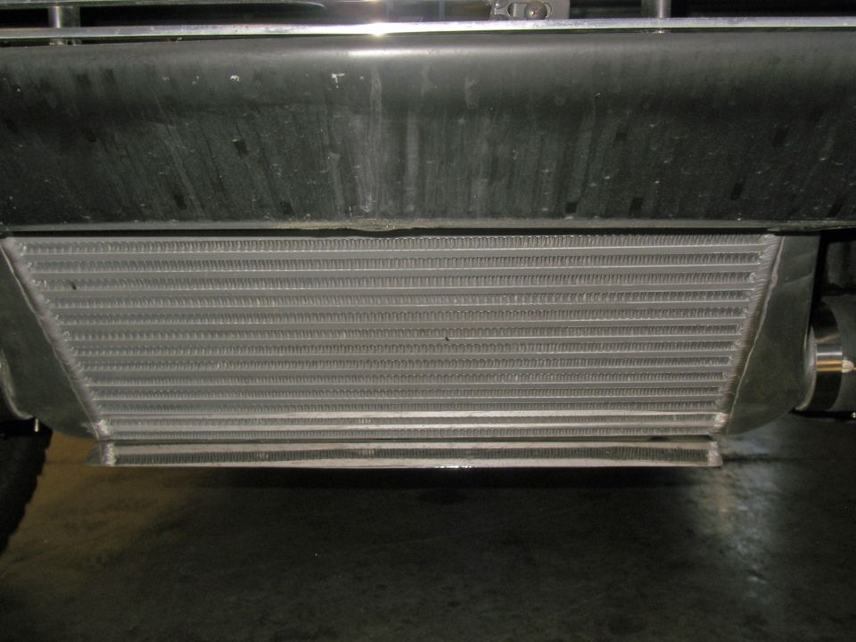 Intercooler mounted below a black bumper and chrome grille. Visible tire on the left