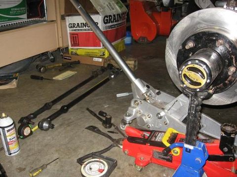 1993 Ford Bronco - Various automotive parts and tools are spread across the floor, including steering components and a brake rotor.