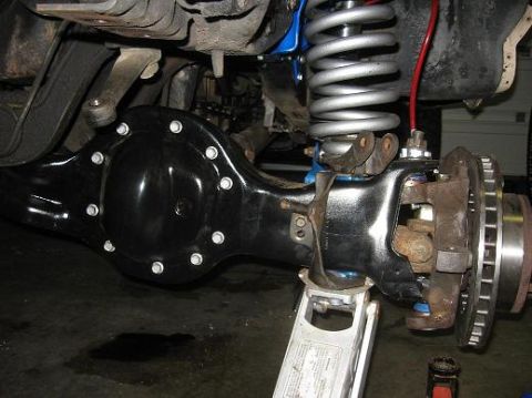 1993 Ford Bronco - Close-up view of a vehicle's rear axle and suspension components, supported by a jack.
