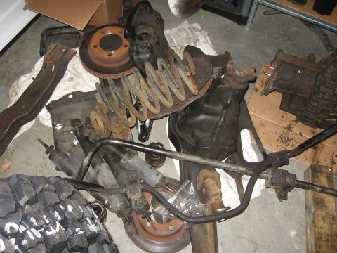 1993 Ford Bronco - Assorted used vehicle suspension parts are piled on the floor, including springs, shocks, and brake rotors.