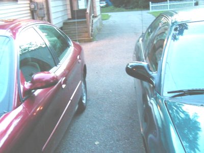 1997 Ford Taurus - Two cars are parked side-by-side in a residential driveway.