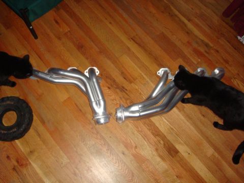 1989 Ford Bronco - Two exhaust headers are shown on a wooden floor, with two black cats interacting with the parts.