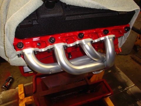 1989 Ford Bronco - Close-up of an engine block with newly installed exhaust headers, resting on a stand.