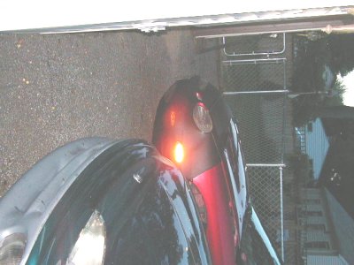 1997 Ford Taurus - Rear view of a dark car, showing an illuminated red taillight and part of the trunk.