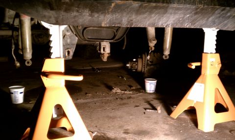 1990 Ford Bronco - Undercarriage of a vehicle is raised on jack stands, revealing suspension and brake parts.