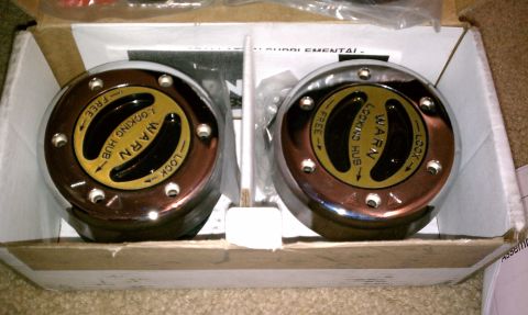 1990 Ford Bronco - Two chrome Warn locking hubs are shown in their packaging, ready for installation on a vehicle.