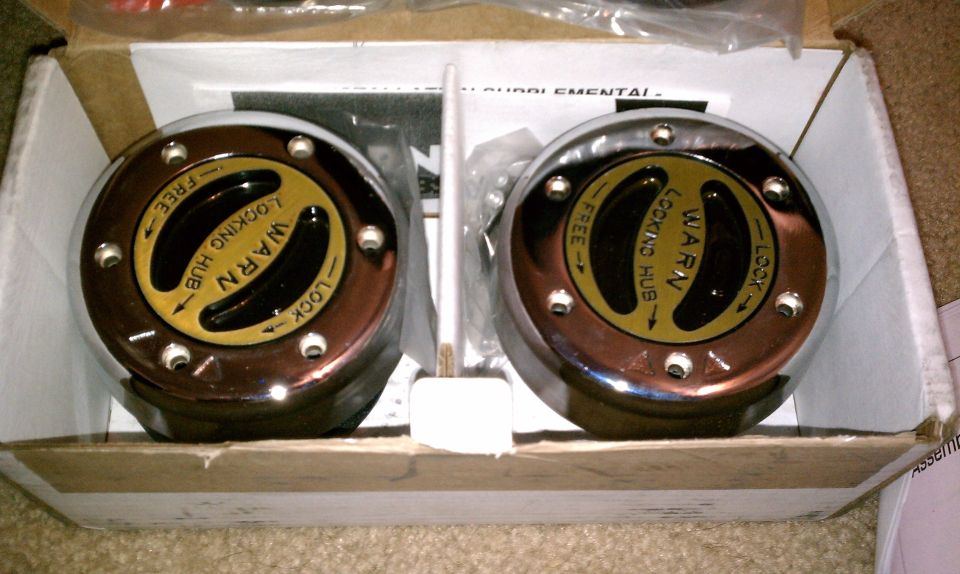 Pair of chrome Warn locking hubs with yellow and black dials in a cardboard box