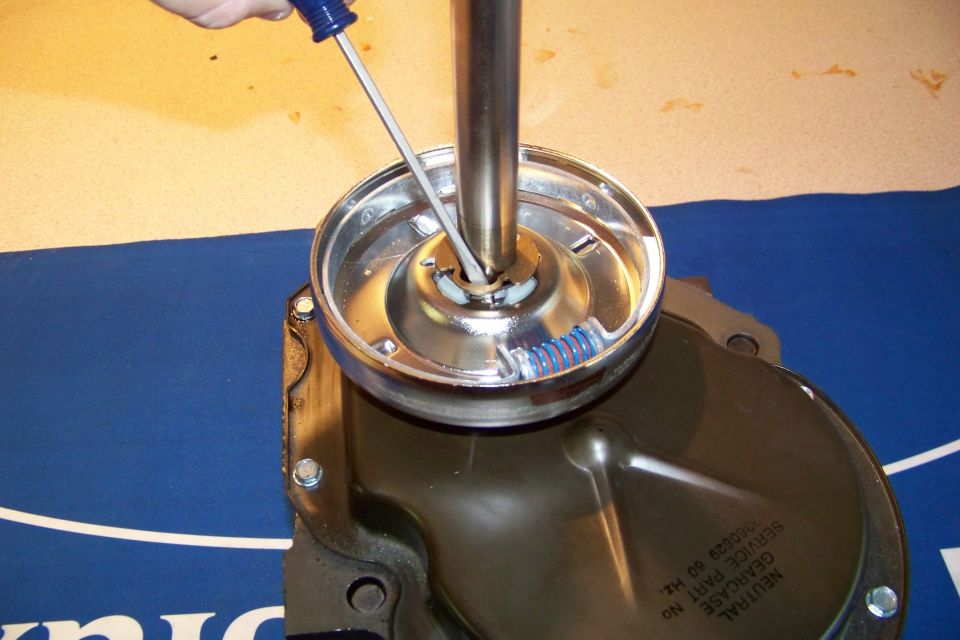 hand using screwdriver on shiny metal part with blue spring, over dark metal casing
