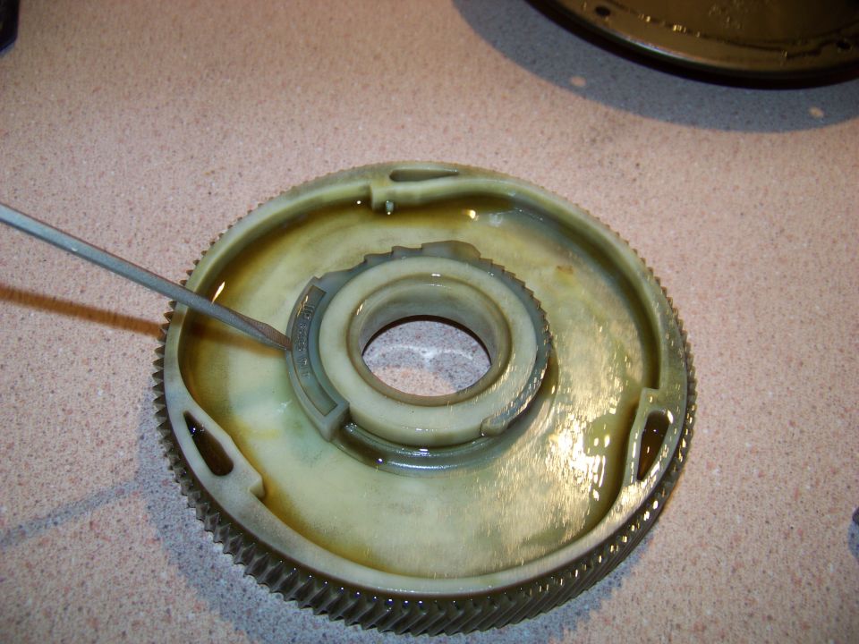 Close-up of a gear with a screwdriver touching it, sitting in some fluid