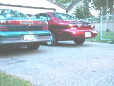 1997 Ford Taurus - Two sedans, one red and one green/red, are parked in a driveway. The red sedan appears to be a 1996 model.