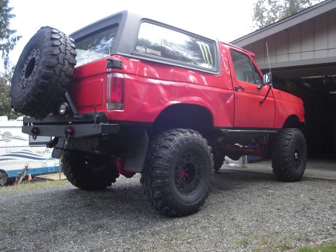 1989 Ford Bronco - This red 1987 Ford Bronco features significant off-road modifications, including a lifted suspension and oversized tires.
